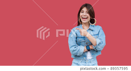 Portrait of happy excited beautiful brunette young woman with makeup in denim casual style standing, amazed, pointing at copyspace and looking at camera. indoor studio shot, isolated on red background Portrait of happy excited beautiful brunette young woman with makeup in denim casual style standing, amazed, pointing at copyspace and looking at camera. indoor studio shot, isolated on red background 89357595