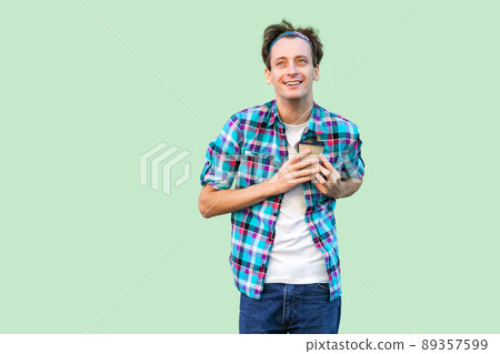 No life without coffee. Handsome young adult hipster man in white t-shirt and checkered shirt holding paper cup with morning coffee and showing love and press to heart. Indoor, isolated, studio shot No life without coffee. Handsome young adult hipster man in white t-shirt and checkered shirt holding paper cup with morning coffee and showing love and press to heart. Indoor, isolated, studio shot 89357599