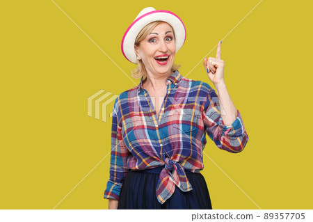 The best idea. Portrait of excited happy modern stylish mature woman in casual style with hat standing, looking at camera with good plan surprised. indoor studio shot isolated on yellow background. 89357705