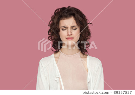 Closeup portrait of alone sad depressed beautiful brunette young woman with curly hairstyle in casual style standing with closed eyes and crying. indoor studio shot isolated on pink background. 89357837