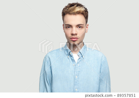 Portrait of calm serious handsome young man in light blue shirt standing and looking at camera with serious face. indoor studio shot on grey background copy space. 89357851