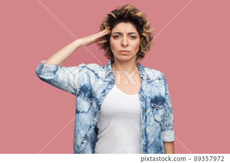 Yes sir. Portrait of serious young worker woman with curly hairstyle in casual blue shirt standing and looking at camera with salute and ready to do smoething. studio shot, isolated on pink background 89357972
