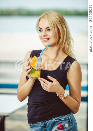 Blond girl on a summer terrace in a bar drinks cocktail 89358022