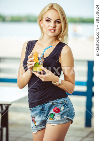 Blond girl on a summer terrace in a bar drinks cocktail 89358024