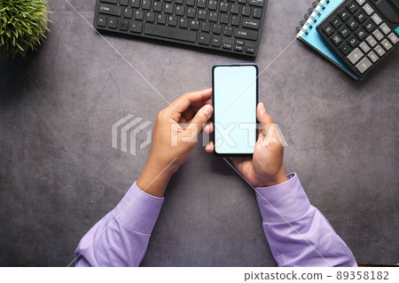 Top view of man hand holding smart phone with empty screen on office desk  89358182