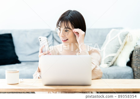 Young woman with glasses using a smartphone during telework Young woman with glasses using a smartphone during telework 89358354