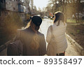 Back view portrait of two women walking and talking in a park asunny day 89358497