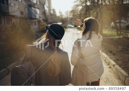 Back view portrait of two women walking and talking in a park asunny day 89358497