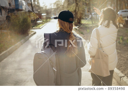 Back view portrait of two women walking and talking in a park asunny day 89358498