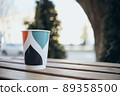 Paper cup with tea coffee drink on a wooden table against the background plant and a green wall. Zero West Concept. 89358500