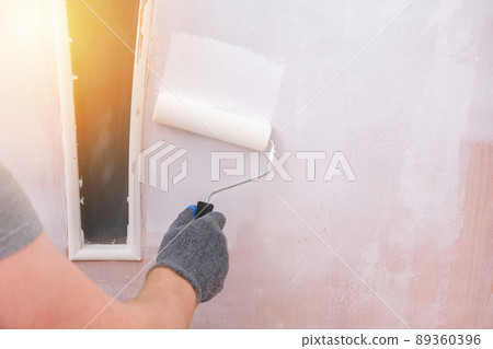 A man paints wooden door white. The painter uses a A man paints wooden door white. The painter uses a 89360396