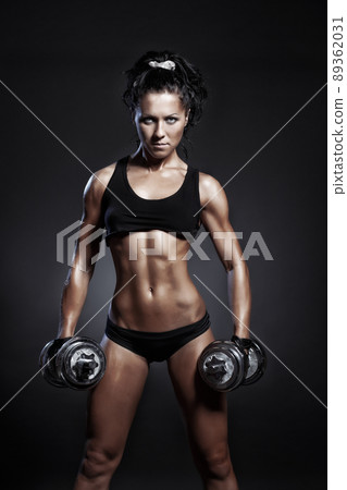 Female fitness model posing with dumbbells on black background Female fitness model posing with dumbbells on black background 89362031