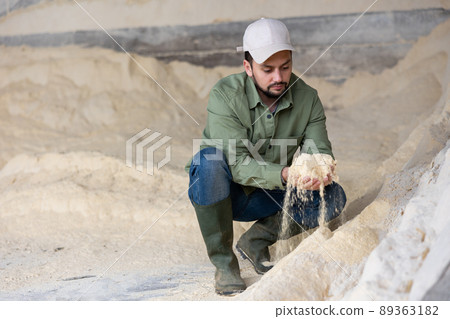 Farmer squatting at heap of corn flour 89363182