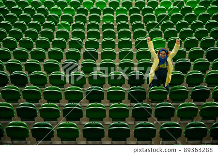 Caucasian woman cheers for a sports team at the stadium. The girl watches the match at the stadium alone. 89363288