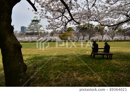 Osaka Castle Park in spring in Japan, cherry blossoms in full bloom and a magnificent castle tower, tourists sitting on a bench and watching cherry blossoms Osaka Castle Park in spring in Japan, cherry blossoms in full bloom and a magnificent castle tower, tourists sitting on a bench and watching cherry blossoms 89364021