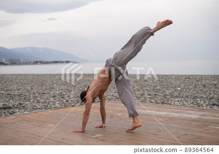 Shirtless caucasian man doing acrobatic wheel on the beach.  89364564