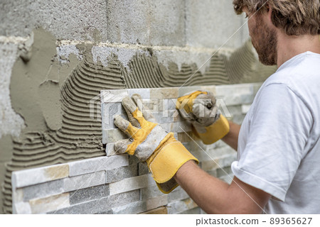 Man pressing an ornamental tile into a glue on a wall Man pressing an ornamental tile into a glue on a wall 89365627