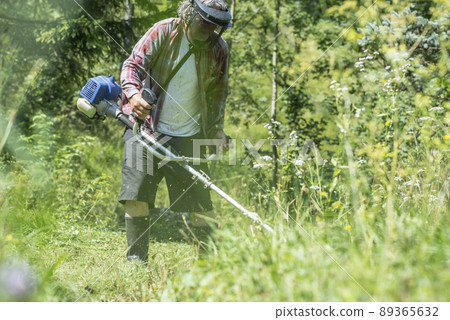 Man with protective headwear and goggles trimming the lawn Man with protective headwear and goggles trimming the lawn 89365632