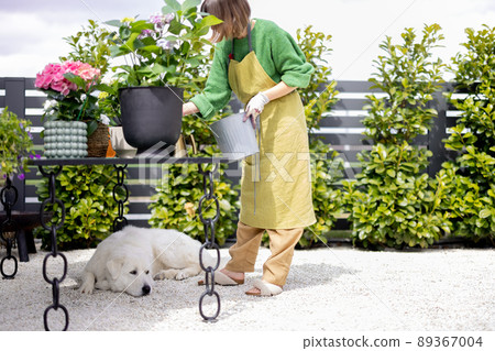 Young woman taking care of flowers with dog in the garden 89367004