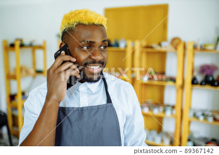 afro male potter talking on the phone in his studio 89367142