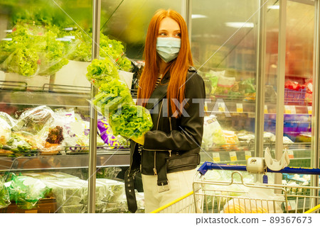 redhaired ginger woman in casual black leather jacket buying fruits orange lettuce in empty super market second wave 89367673