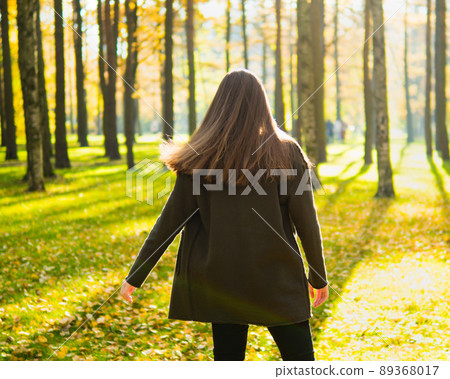 Girl with long dark hair is spinning in Park in sunlight. Woman stands with her back, facing sun, looking forward 89368017