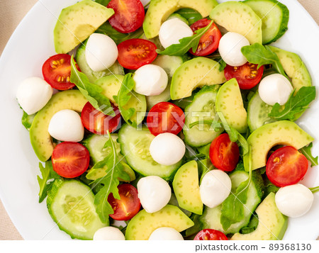 Fresh salad - tomatoes, cucumbers, arugula, mozzarella, avocado. Oil with spices, rosemary thyme, top view, close up Fresh salad - tomatoes, cucumbers, arugula, mozzarella, avocado. Oil with spices, rosemary thyme, top view, close up 89368130