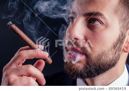 Portrait of an attractive business man with a cigar in black background studio Portrait of an attractive business man with a cigar in black background studio 89368419