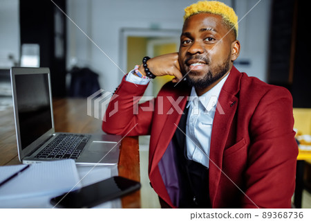 african american person sitting at office typing message note on phone near laptop 89368736