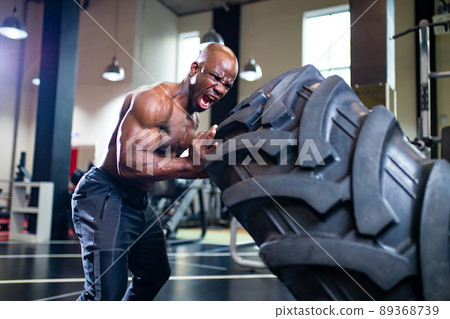 bare torso mexican man effort flipping the wheel in dark gym 89368739