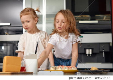 Two little girls siblings having fun and eating on the kitchen at home with japanese food. Two little girls siblings having fun and eating on the kitchen at home with japanese food. 89370448