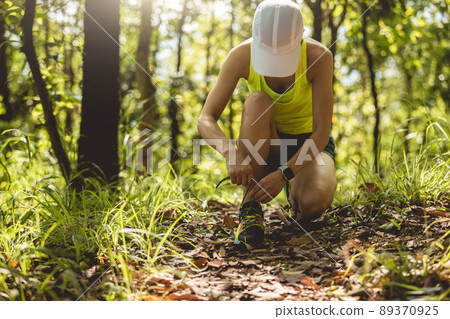 Woman runner tying shoelace on forest trail Woman runner tying shoelace on forest trail 89370925