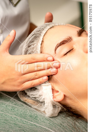 Head massage. Beautiful caucasian young white woman receiving a head and forehead massage with closed eyes in a spa salon Head massage. Beautiful caucasian young white woman receiving a head and forehead massage with closed eyes in a spa salon 89370978