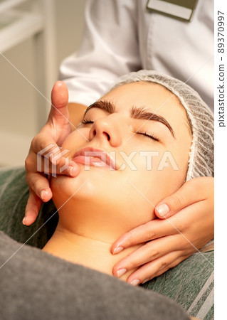 Face massage. Beautiful caucasian young white woman having a facial massage with closed eyes in a spa salon 89370997