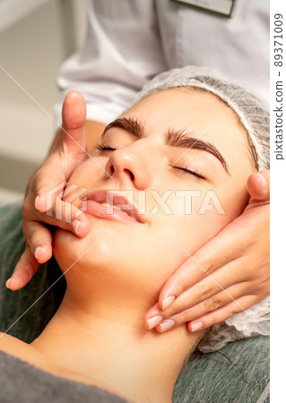 Face massage. Beautiful caucasian young white woman having a facial massage with closed eyes in a spa salon Face massage. Beautiful caucasian young white woman having a facial massage with closed eyes in a spa salon 89371009