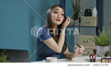 Asian content creator testing mascara product on vlogging camera, filming beauty tutorial with makeup tips. Asian woman doing glam cosmetics recommendation, online social media broadcast. 89372370