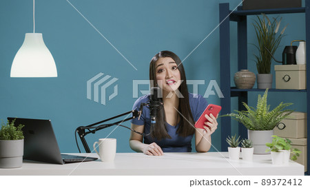 POV of content creator reading comments on camera, answering questions with smartphone. Female vlogger filming video for social media channel, using mobile phone. Tripod shot. POV of content creator reading comments on camera, answering questions with smartphone. Female vlogger filming video for social media channel, using mobile phone. Tripod shot. 89372412