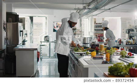 African american chef slicing fresh celery on cutting board, preparing ingredients for gourmet meal and culinary food recipe. Male cook using professional utensils to make gastronomy dish. African american chef slicing fresh celery on cutting board, preparing ingredients for gourmet meal and culinary food recipe. Male cook using professional utensils to make gastronomy dish. 89372454