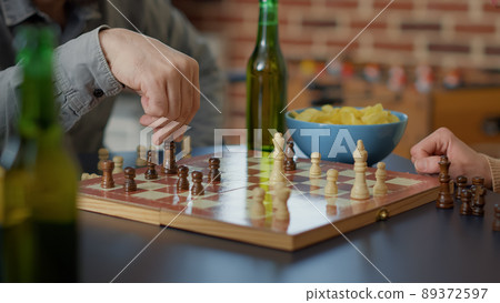 Young people having fun with chess board games play, serving alcoholic drinks and snacks. Group of friends playing match on table for entertainment at gathering. Tripod shot. Close up. Young people having fun with chess board games play, serving alcoholic drinks and snacks. Group of friends playing match on table for entertainment at gathering. Tripod shot. Close up. 89372597