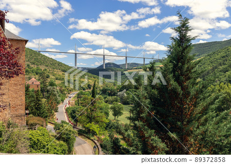 Old valley road D41 enters Peyre village and Millau Viaduct on background. Aveyron, Occitania 89372858