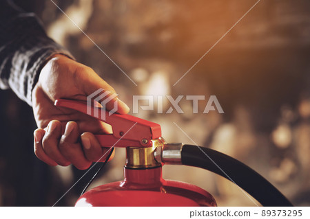 hand presses the trigger fire extinguisher available in fire emergencies conflagration damage background. Safety 89373295