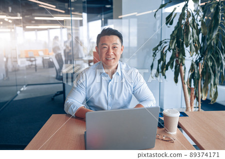 Portrait of smiling Asian businessman working at her workplace in modern office  89374171