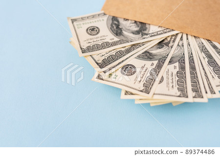 Stash of money in dollar bills coming out of an envelope on a blue background. The concept of salary, bribe, loan, debt, win. Stash of money in dollar bills coming out of an envelope on a blue background. The concept of salary, bribe, loan, debt, win. 89374486
