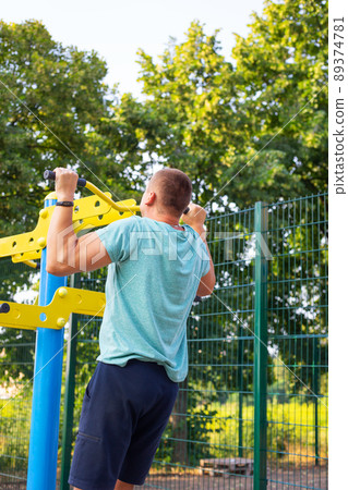 A man is exercising on the street. Opening gym outdoors on the sports ground in a green park. 89374781