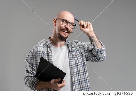 Pensive handsome balded beard with musctache man wearing casual clothes holding clipboard isolated over gray background.  89376559