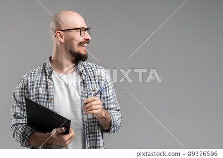 Handsome balded beard with musctache man wearing casual clothes holding clipboard smiling isolated over gray background.  89376596