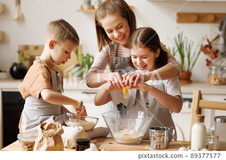 Happy woman and cute children cooking together in kitchen Happy woman and cute children cooking together in kitchen 89377577