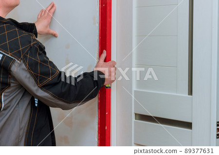 Man hands using red level measuring surface of new white wooden door 89377631