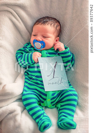 Cute baby with 1 month old milestone card in his hand Cute baby with 1 month old milestone card in his hand 89377642