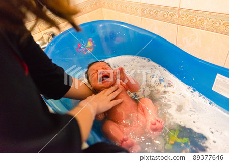 Mother bathes her newborn baby for the first time in a baby bath Mother bathes her newborn baby for the first time in a baby bath 89377646